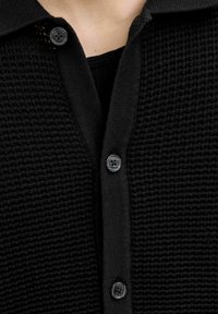 Black cardigan with a textured, knitted fabric. Features a collared neckline and three dark buttons on the front.