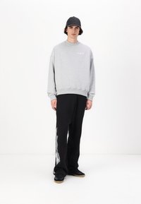 Gray sweatshirt with dropped shoulders, paired with black pants featuring a flame pattern. Black cap and sneakers complete the look.