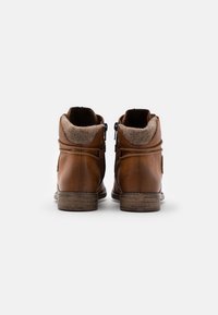 Botas de tobillo de cuero marrón con un suave forro de fieltro marrón, cremallera lateral y cordones decorativos. Equipadas con un tacón texturizado para mayor agarre.