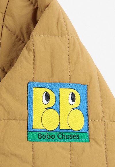 Gros plan sur un tissu marron matelassé avec un patch coloré montrant deux personnages jaunes stylisés et le texte "Bobo Choses."