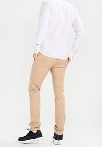 Beige slim-fit pants with a smooth texture, paired with a white button-up shirt featuring a small navy dot pattern, and black sneakers.