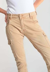 Pantalones cargo beiges con un corte ajustado, que cuentan con múltiples bolsillos, cierre de botón y una suave tela de algodón ligera.