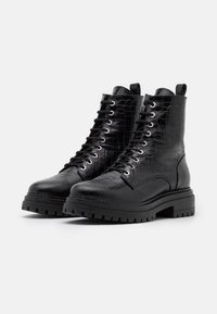 Bottes de combat noires avec une tige en cuir texturé à motif crocodile. Fermeture à lacets, semelle en caoutchouc robuste et languette de tirage à l'arrière.