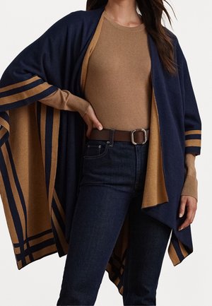 Femme portant un haut à manches longues couleur camel, un jean bleu foncé avec une ceinture marron, et une étole ouverte à rayures bleu marine et camel.