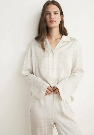 Helle beigefarbene Seiden-Pyjama-Set, das ein Hemd mit Knopfleiste und Kragen sowie einem zarten Karomuster umfasst, kombiniert mit locker sitzenden Hosen und weiten Ärmeln.