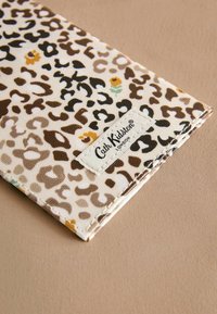 Plånbok med leopardskinnmönster och en tygstruktur, med bruna, svarta och gula fläckar på en krämfärgad bakgrund, med en vit logotyp-flik.