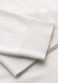 Biała dzianina z prążkowanymi mankietami. Tekstura jest miękka i gładka, z równą, czystą wykończeniem. Prosta i wszechstronna konstrukcja.