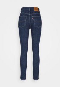 Tmavě modré džíny skinny s vysokým pasem, vybavené zadními kapsami, koženou nášivkou na pase a klasickým pětioktovým designem.