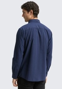 Camicia a quadri blu navy con maniche lunghe, dotata di un colletto strutturato e dettagli con bottoni sui polsini e sul retro.