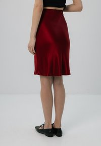 Czerwona satynowa spódnica midi o gładkiej fakturze, lekko rozkloszowanym kroju i elastycznym pasku w talii. Połączona z czarnymi płaskimi butami.