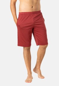 Shorts en coton rouge avec une taille élastique, des poches latérales et une coupe décontractée, se terminant juste au-dessus des genoux. Texture lisse et légère.