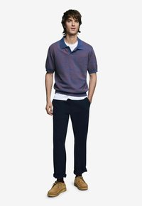 Pletené polo tričko vo fialovom a modrom tónovanom vzore, skombinované s bielym tričkom, námorníckymi nohavicami a svetlohnedými semišovými topánkami.