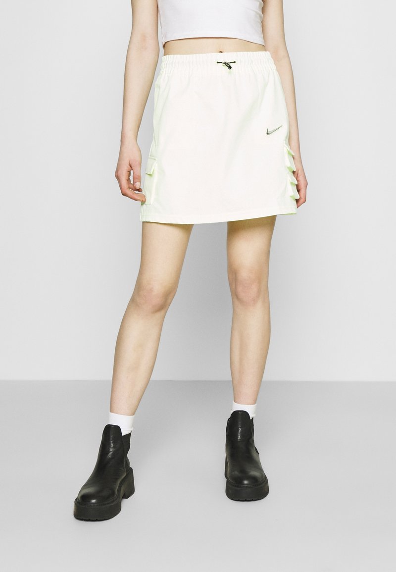 Jasnozielona spódnica Nike z elastycznym paskiem w talii, falbankami po bokach oraz gładką fakturą, zestawiona z czarnymi platformami.