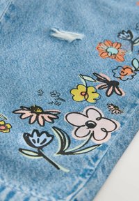 Blauer Denim-Stoff mit verschiedenen floralen Mustern in Pink, Gelb, Hellblau und Grün, mit einer abgenutzten Stelle und strukturiertem Finish.