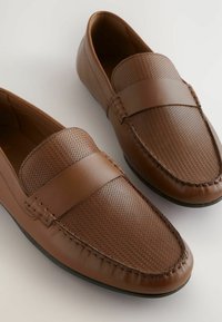 Brune loafers lavet af struktureret læder med et glat bånd over toppen. Har stikninger langs kanterne og et rundt tådesign.