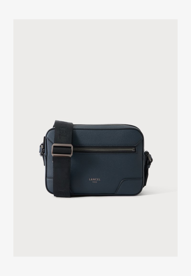 Тъмносиня чанта за носене през рамо Lancel Paris с черна презрамка, преден джоб с цип и метални елементи със сребристо покритие на изчистен фон.