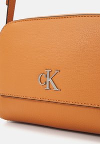 Orange leather handbag featuring a textured surface, silver logo "cK," and contrasting stitching along the edges.