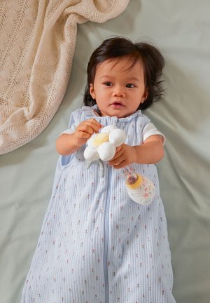 Light blue sleeping bag with floral patterns, soft fabric, and a zipper. Child holds a plush flower and a clear bottle with floral design.