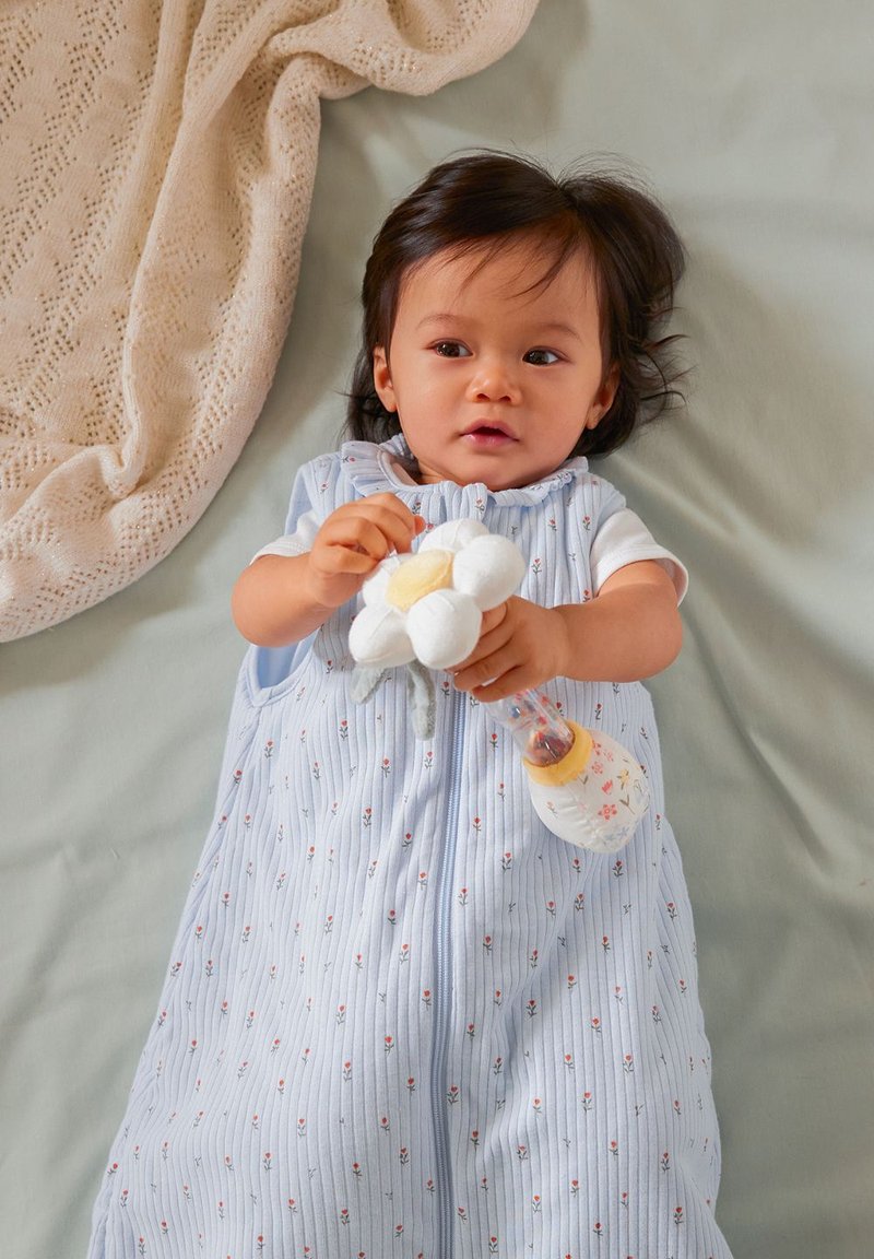 Helles blaues Schlafsack mit Blumenmustern, weicher Stoff und einem Reißverschluss. Kind hält eine plüschige Blume und eine klare Flasche mit Blumendesign.