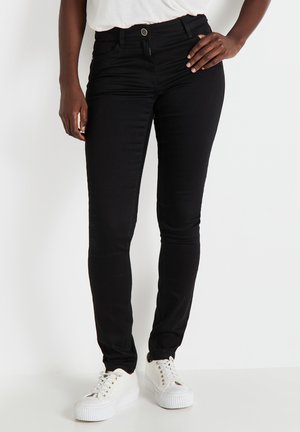Jeans skinny negros con una textura suave y un diseño ajustado, que cuentan con una cremallera y cierre de botón, combinados con zapatillas de plataforma blancas.