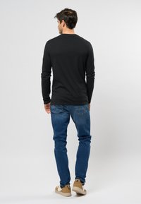 Camicetta nera a maniche lunghe, jeans blu e scarpe beige. La camicia ha un design semplice; i jeans sono aderenti con uno stile classico a cinque tasche.