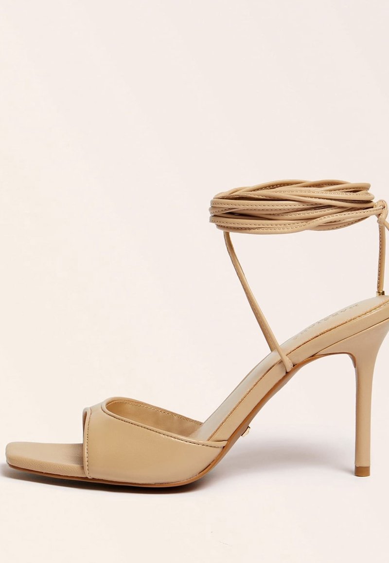 Sandale beige à talon haut, bout ouvert, bride de cheville et talon stiletto fin sur fond uni clair.