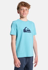 Ανοιχτό μπλε βαμβακερό T-shirt με σκούρο μπλε λογότυπο κύματος βουνού στο στήθος. Κοντά μανίκια, στρογγυλή λαιμόκοψη και άνετη εφαρμογή.