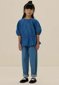 Haut en denim avec des manches bouffantes ornées de cœurs bleus brodés ; associé à un jean bleu large retroussé aux poignets et des chaussures noires.