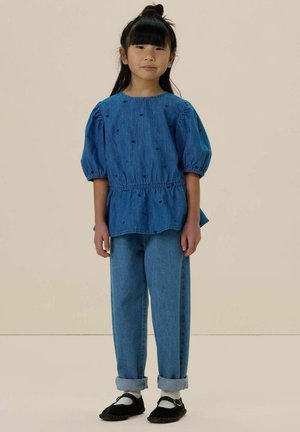 Denim top met opgezette mouwen met blauwe geborduurde harten; gecombineerd met losse blauwe jeans met opgerolde pijpen en zwarte schoenen.