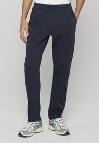 Pantalon de jogging bleu marine en tissu doux, avec une ceinture élastique à cordon de serrage, des poches latérales et une coupe fuselée.