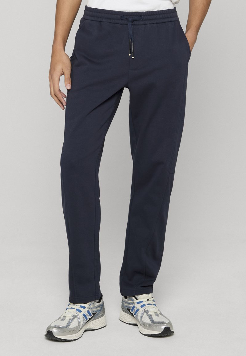 Pantalon de jogging bleu marine en tissu doux, avec une ceinture élastique à cordon de serrage, des poches latérales et une coupe fuselée.