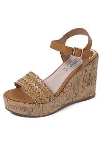 Sandalo con zeppa color nocciola con suola in sughero, cinturino superiore intrecciato e fibbia alla caviglia. Texture di pelle liscia con design a punta arrotondata.