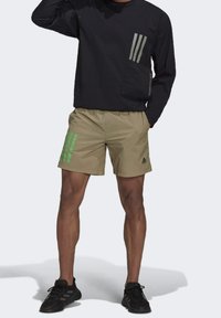 Svart långärmad tröja med grå ficka och tre ränder; khaki-shorts med gröna ränder och Adidas-logotyp; svarta träningsskor.