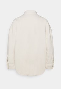 Jasno-beżowa bawełniana koszula z kołnierzykiem, luźny krój i zapięcia na guziki. Gładka tekstura i zakrzywiony dół, minimalistyczny design.