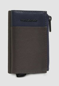 Portafoglio in pelle marrone e blu navy con tasca con cerniera, superficie texturizzata e dettaglio con marchio impresso. Design rettangolare, dimensioni compatte.