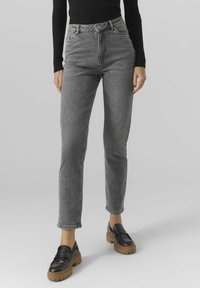 Jeans de talle alto en gris con corte ajustado, hechos de denim, que cuentan con cinco bolsillos y un cierre de botón resistente, combinados con mocasines de plataforma negros.