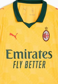 Žltý futbalový dres so zeleným golierom, s červeným logom Puma, textom "Emirates FLY BETTER" v tmavozelenej farbe a insigniou AC Milanu.