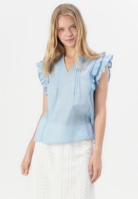 Blusa de manga corta azul claro con acentos de volantes, con cuello en V, tejido texturizado y detalles de pliegues en la parte frontal.