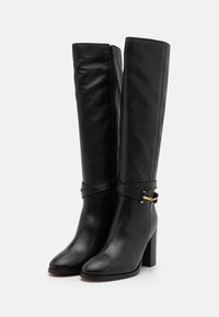 Bottes en cuir noir, montant jusqu'au genou, avec un bout carré, un talon large et des accents en métal doré. Elles possèdent une fermeture éclair sur le côté et un détail de sangle enroulée.