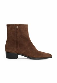 Stivale alla caviglia in suede marrone con punta affusolata, tacco nero basso e una accentatura in hardware dorato sulla linguetta posteriore. Texture liscia, design minimalista.