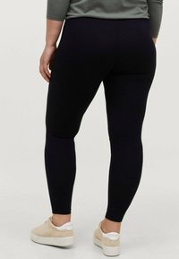 Black leggings made of stretchy fabric, featuring a fitted cut that tapers at the ankle. Worn with beige sneakers and a gray top.