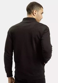 Czarny sweter z dzianiny z wysokim kołnierzem, teksturowana tkanina oraz ściągacze przy rękawach i u dołu, wyróżniający się minimalistycznym wzornictwem bez widocznych logo.