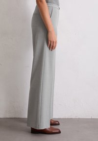 Pantaloni grigi chiari a vita alta con design dritto e texture senza cuciture, abbinati a stivaletti marroni alla caviglia. Bottone e tasche visibili.