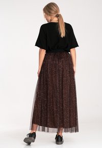 Czarny top z krótkim rękawem i długa, brązowa, przezroczysta spódnica w panterkę. Czarne sneakersy dopełniają strój, ukazując warstwową teksturę.