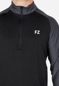 Svart idrottspullover med dragkedja i kragen, med en texturerad grå randdesign på axlarna och en vit "FZ"-logotyp på bröstet.