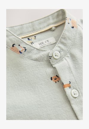 Svetlo zelena majica iz blaga z zapenjanjem ovratnika na gumbe, z vzorci risanih psov v oranžni in črni barvi. Oznaka pravi "NEXT."