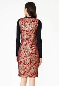 Robe avec une coupe ajustée, présentant des manches longues noires et un dos rouge recouvert de motifs en feuille d'or. Texture lisse avec des accents brillants.