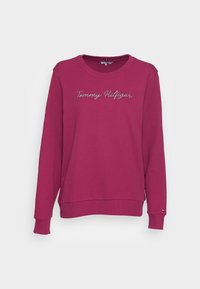 Sudadera burdeos con mangas largas y un cuello redondo. Presenta el texto bordado "Tommy Hilfiger" en plata, puños acanalados y dobladillo.