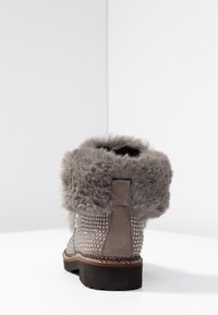 Botte de cheville grise avec un revers en fausse fourrure, design clouté sur les côtés et semelle en caoutchouc noire. Présente un dessus texturé et des coutures marron.