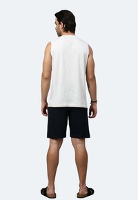 Weißes ärmelloses Hemd, dunkle Shorts und schwarze Sandalen. Das Hemd hat ein schlichtes Design; die Shorts sind knielang und aus Stoff.